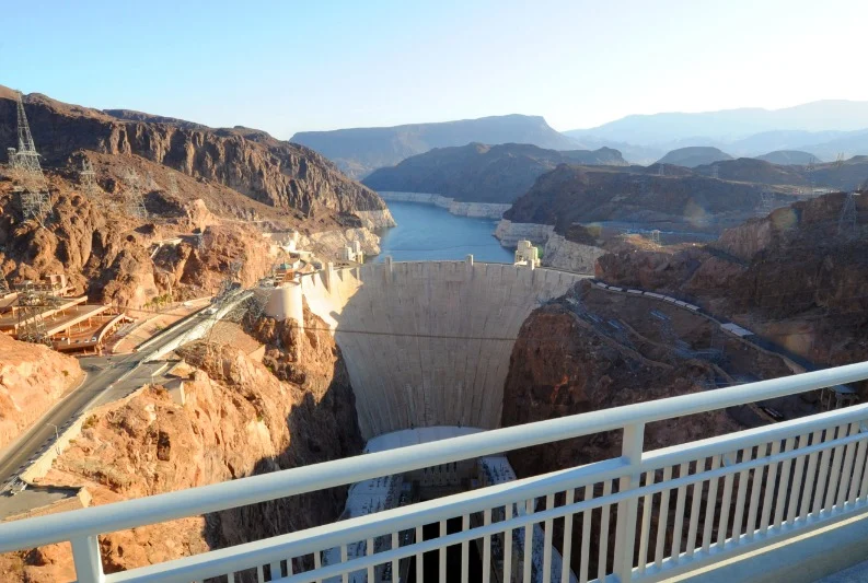 Uitzicht vanaf een metalen loopbrug op de Hoover Dam die de rotsachtige kloof afsluit met het blauwe water van het stuwmeer erachter