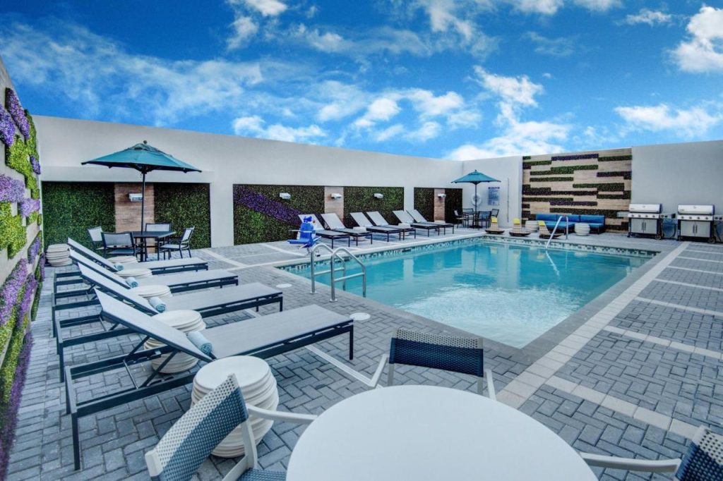 Hotelzwembad op een dakterras omringd door loungestoelen, parasols en een muur begroeid met kunstplanten