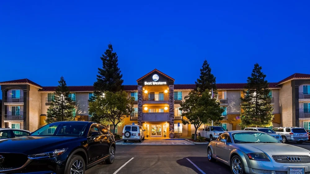 Driehoog hotelgebouw met verlichte gevel en het opschrift Best Western staat achter een parkeerplaats vol auto's onder een donkerblauwe avondlucht