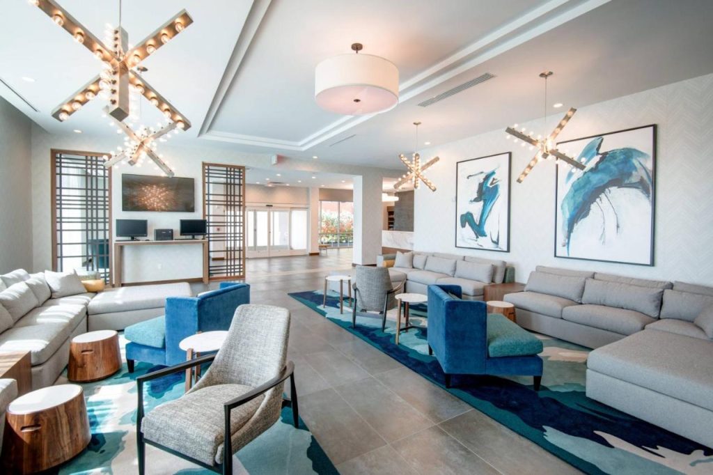Moderne hotellobby met grijze banken, blauwe fauteuils en stervormige hanglampen boven een blauw tapijt