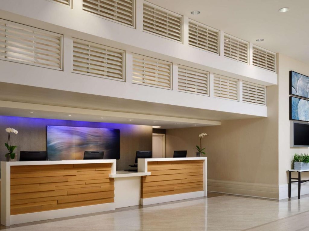 Houten receptiebalie met twee computerschermen in een lichte lobby met een blauw verlicht scherm op de achtergrond