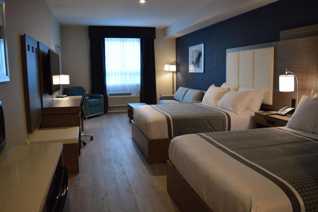 Ruime hotelkamer met twee opgemaakte bedden, een blauwe accentwand, een bureau met stoel en een lounge stoel bij het raam