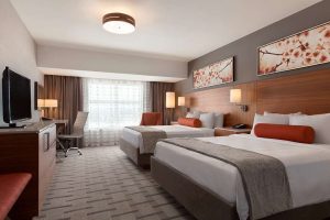 Moderne hotelkamer met een opgemaakt bed met rode sierkussens, kersenbloesem schilderijen aan de muur en een televisie op een houten dressoir