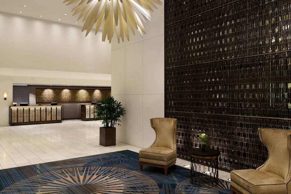 Een moderne hotellobby met een stervormige gouden lamp, leren loungestoelen en een muur van donker metalen rooster