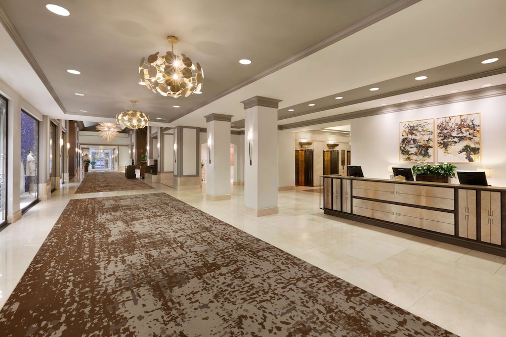 Een lichte hotellobby met een gouden kroonluchter, marmeren vloer en een receptiebalie met kunstwerken aan de muur