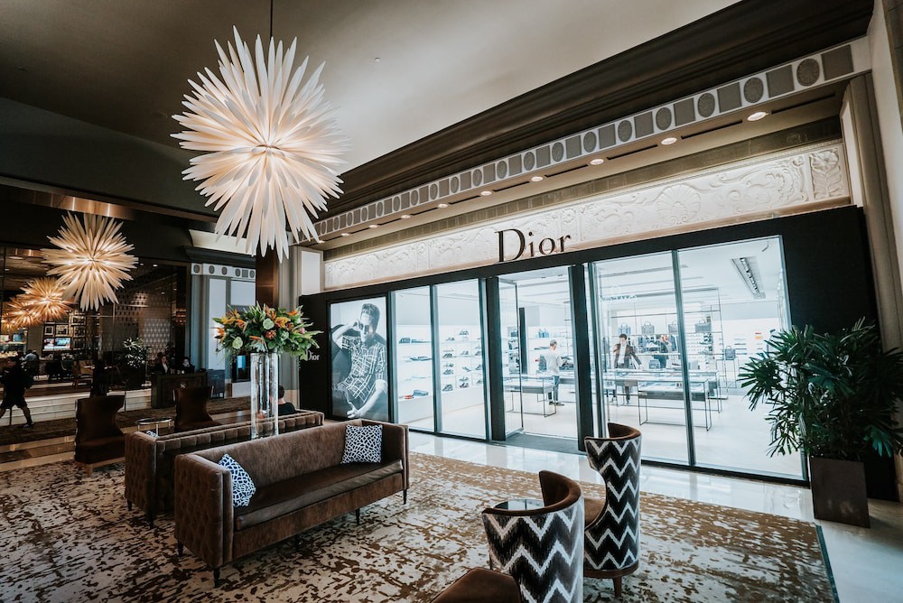 Een hotellobby met banken, fauteuils en witte sterkroonluchters bij een verlichte winkelpui met etalage