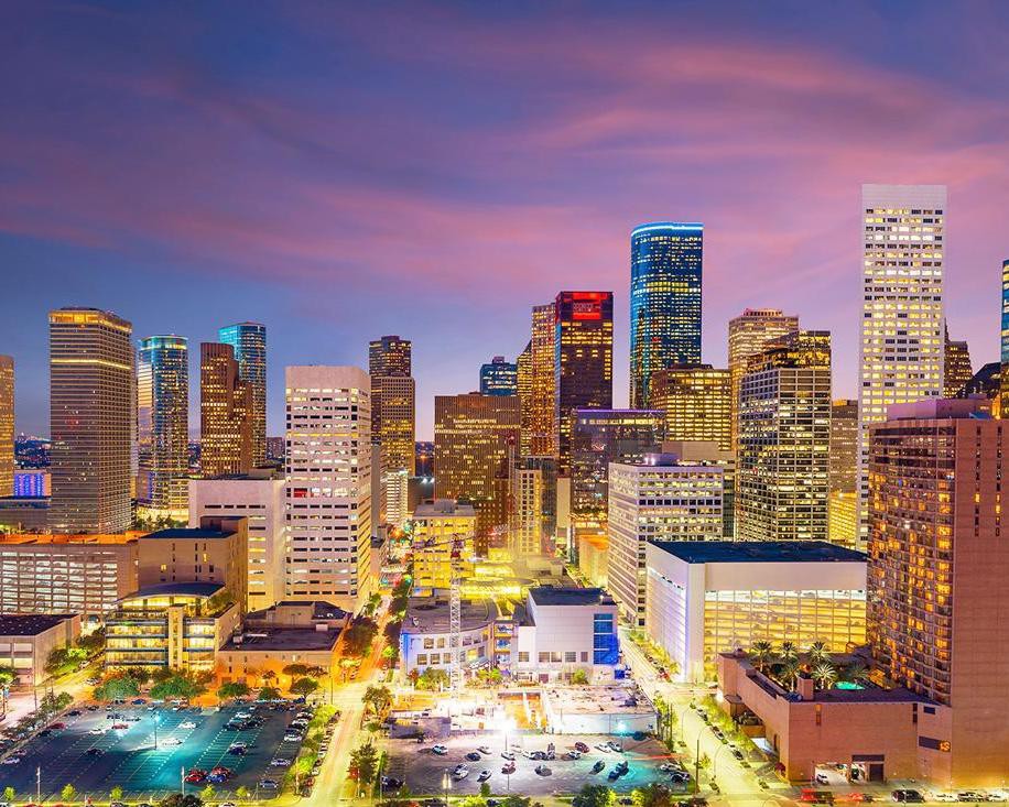Verlichte wolkenkrabbers van het centrum van Houston tegen een paarsroze avondlucht bij zonsondergang