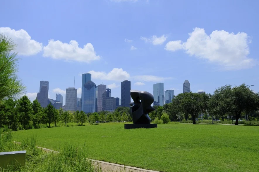 Grote abstracte zwarte sculptuur op een grasveld, met de wolkenkrabbers van Houston op de achtergrond onder een blauwe lucht