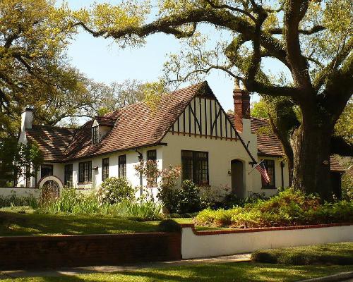 Wit gepleisterd huis met donker houtwerk in Tudorstijl en een rood pannendak, gedeeltelijk verscholen achter een grote oude eik