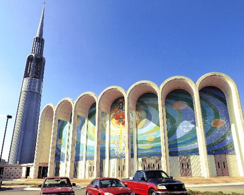 Modern kerkgebouw met een hoge spitse toren en gebogen gevels met kleurrijke mozaïekramen onder een strakblauwe lucht in Huntsville