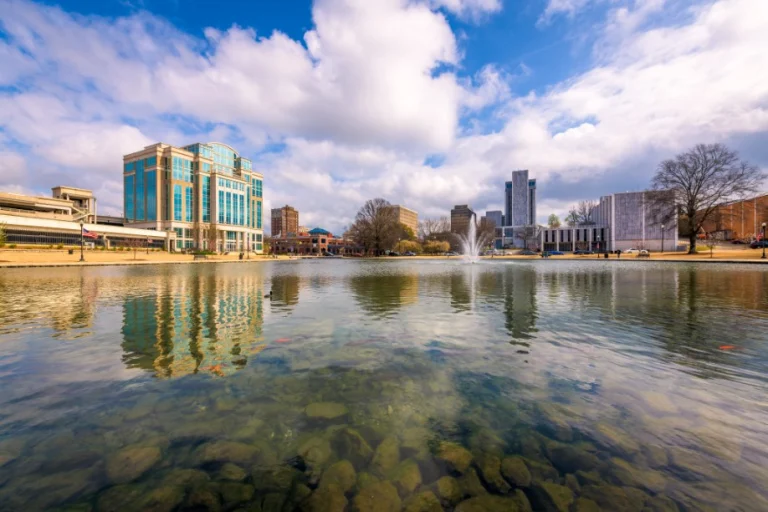 De skyline van Huntsville in Alabama weerspiegelt in een vijver met een fontein en heldere lucht met wolken
