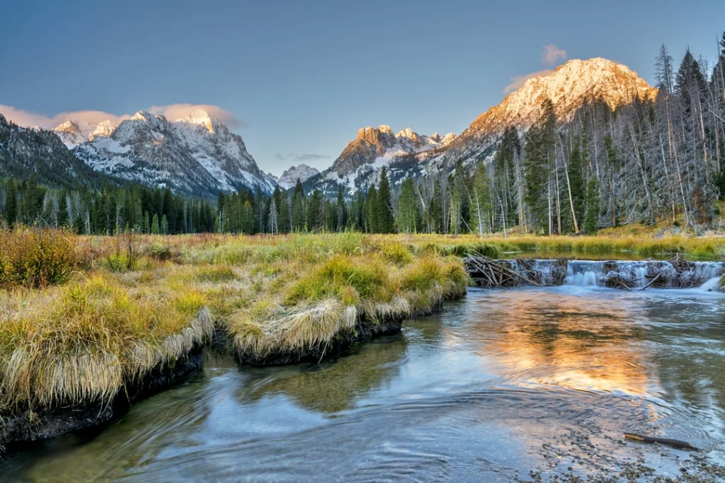 Kronkelende beek in een grasveld met besneeuwde bergtoppen die oplichten bij zonsopkomst in Idaho