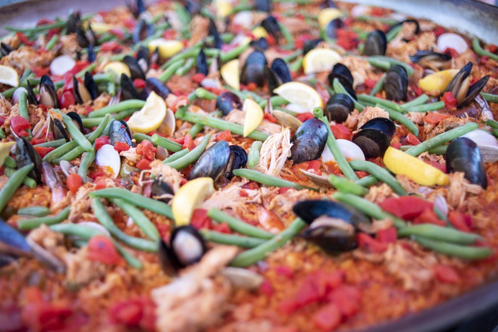 Close-up van een grote pan paella met mosselen, sperziebonen, citroen, tomaat en stukjes vlees