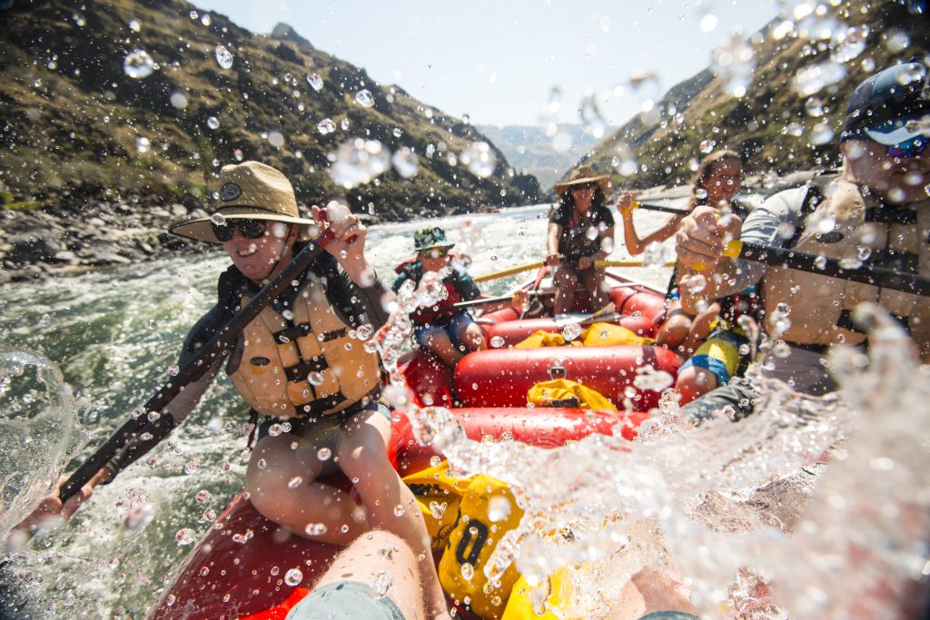 Groep in reddingsvesten en helm vaart in raften door wit water in een nauwe kloof met steile rotswanden