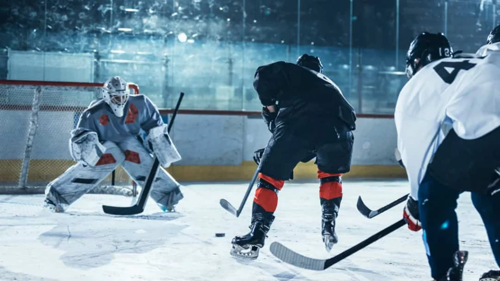 Keeper in wit beschermend tenue houdt de wacht bij het doel terwijl spelers om de puck strijden