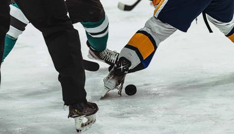 Close-up van de schaatsen en sticks van meerdere spelers die om de zwarte puck strijden op het ijs