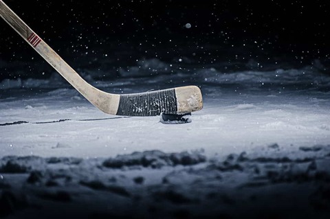 Close-up van een ijshockeystick die de zwarte puck op het ijs raakt tegen een donkere achtergrond met sneeuwvlokken