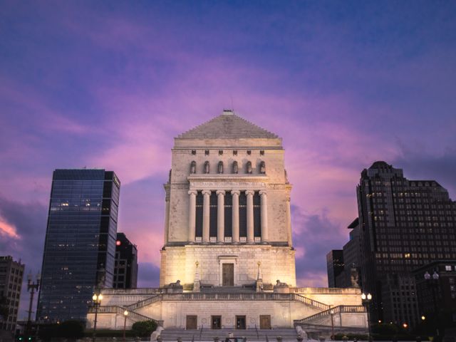 Verlicht Indiana War Memorial met zuilen en een piramidevormig dak tussen wolkenkrabbers onder een paarse avondlucht in Indianapolis