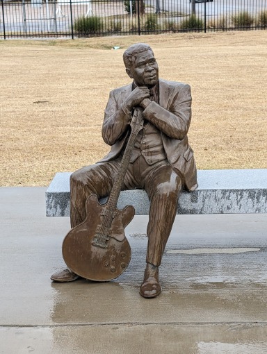 Bronzen standbeeld van een zittende man in pak met een gitaar tegen zijn been in Indianola, Mississippi
