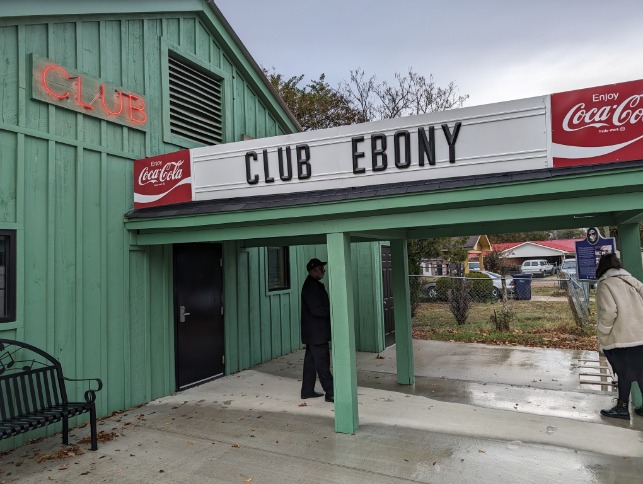 Groen houten gebouw met het bord Club Ebony en Coca-Cola reclames aan de gevel met bezoekers ervoor in Indianola, Mississippi
