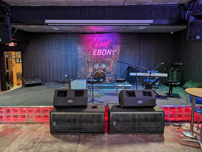 Leeg podium met drumstel, keyboard en versterkers onder een neonbord met de tekst Club Ebony in Indianola, Mississippi