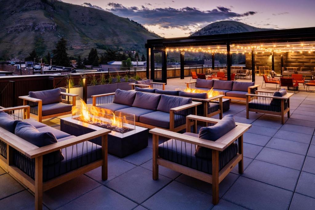 Dakterras met loungebanken rond brandende vuurplaatsen, lichtjes in een pergola en uitzicht op bergen bij zonsondergang