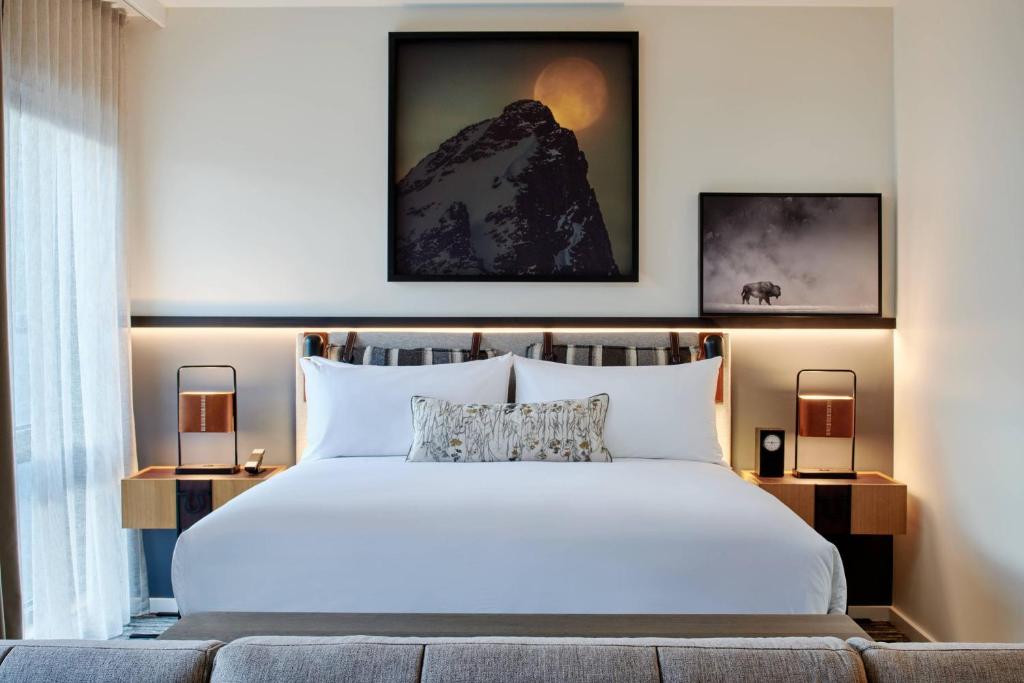 Hotelkamer met een groot wit bed, een ingelijste foto van een besneeuwde bergtop erboven en een kleinere foto van een bizon in de mist