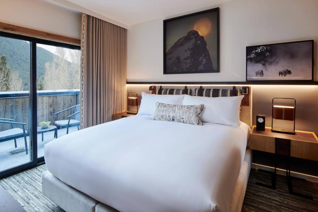 Hotelkamer met een groot bed en een schuifdeur naar een terras met stoelen en uitzicht op de bergen