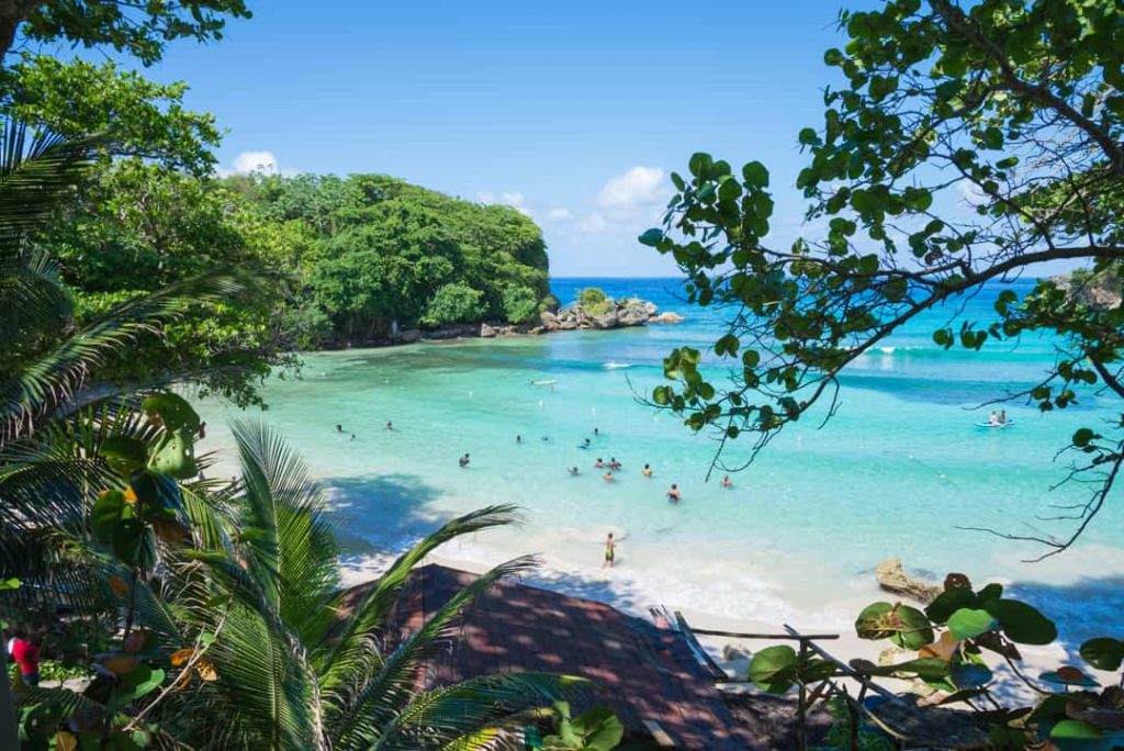 Zwemmers genieten van helder turkoois water in een beschutte baai met wit strand omringd door groene begroeiing in Jamaica