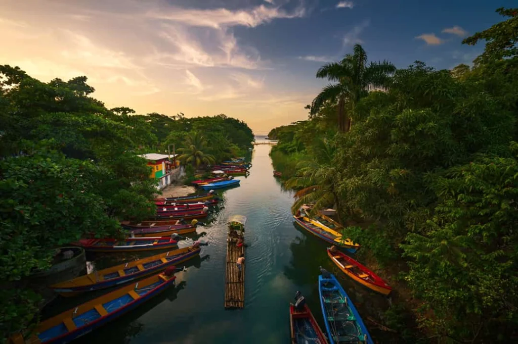 Kleurrijke bootjes liggen afgemeerd op een rustige rivier omzoomd door palmbomen bij zonsondergang nabij Ocho Rios op Jamaica