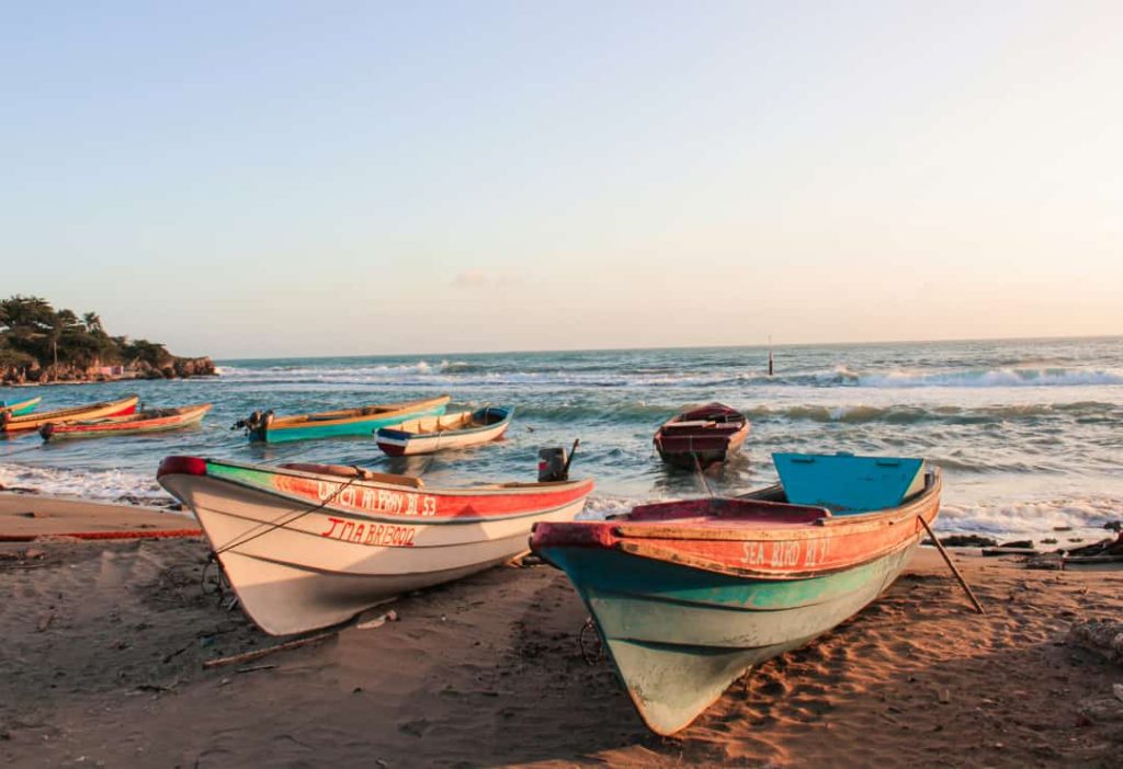 Kleurrijke houten vissersboten liggen op het zandstrand van Jamaica terwijl de golven aanrollen bij zonsondergang