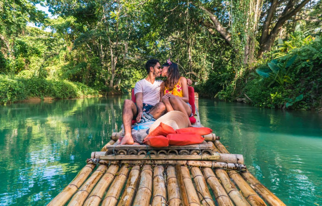 Een verliefd stel zit te knuffelen op een bamboevlot met rode kussens op een groene rivier tussen jungle in Jamaica