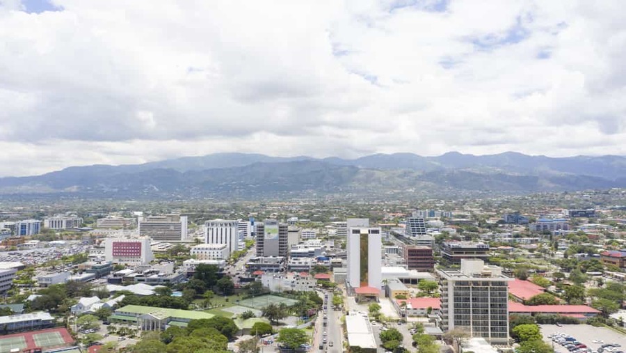 Luchtfoto van Kingston in Jamaica met moderne kantoorgebouwen, woonwijken en een groen berglandschap onder een bewolkte lucht