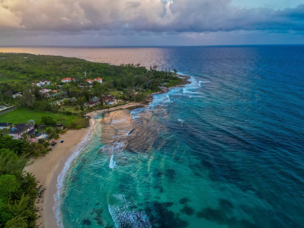 Luchtfoto van een strand met huizen en een koraalrif onder een dramatische bewolkte lucht in Jamaica