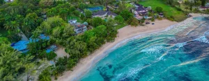 Luchtfoto van een weelderige groene kustlijn op Jamaica met luxe villa's tussen palmbomen, een wit zandstrand en helder turquoise water