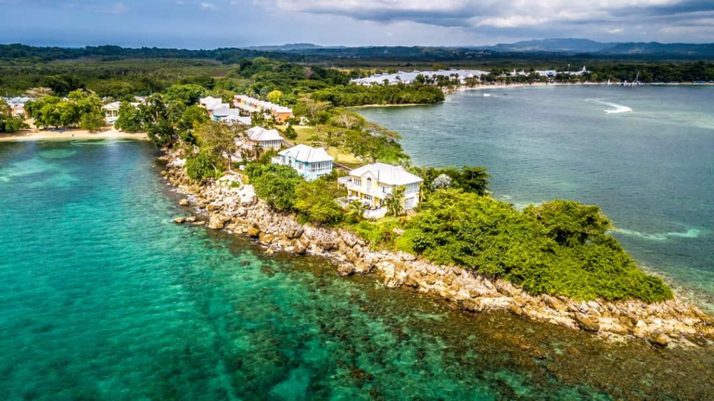 Luchtfoto van een rotsachtig schiereiland met witte villa's tussen groen gebladerte, omringd door helder turquoise water