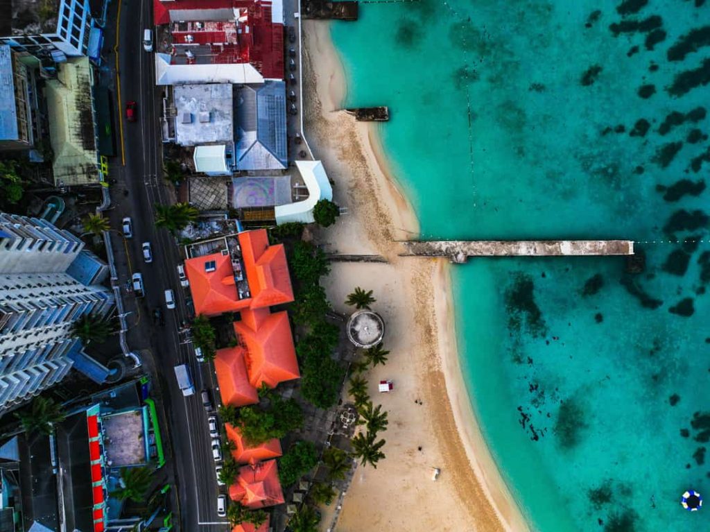 Luchtfoto van rode daken, een strand en een lange steiger die de zee in steekt bij een kustplaats in Jamaica