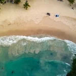 Luchtfoto van boven op een zandstrand tussen groene jungle waar witte golven breken op de kust van Jamaica