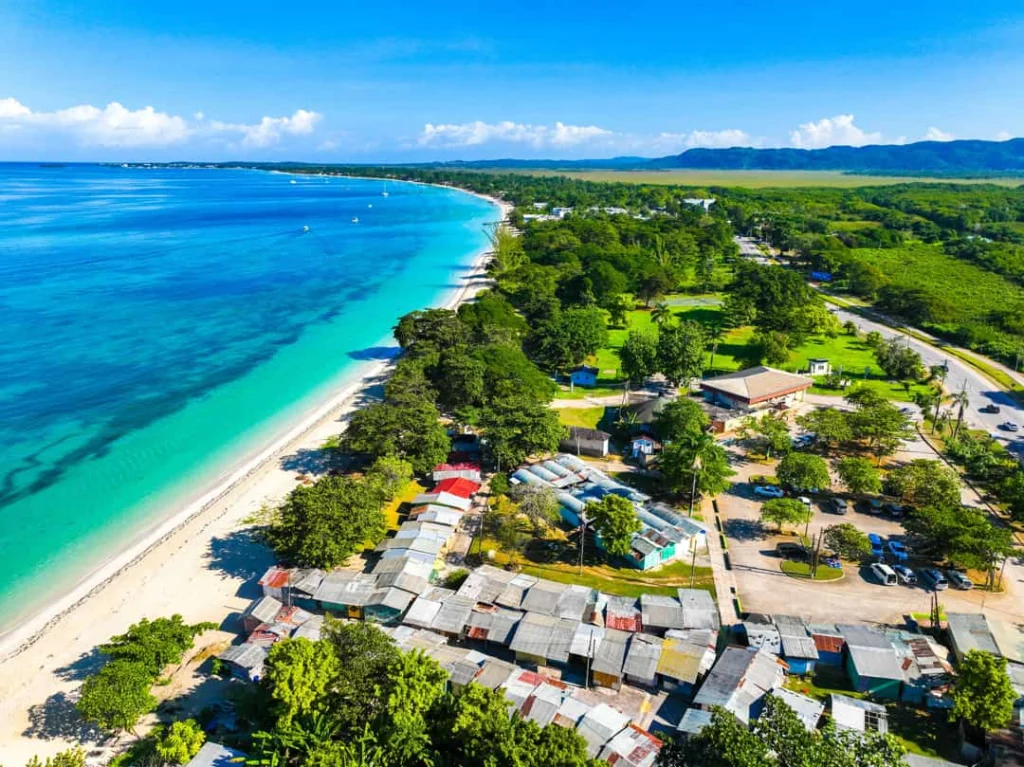 Luchtfoto van een lang wit zandstrand met turquoise water en bebouwing tussen het groen bij Negril op Jamaica