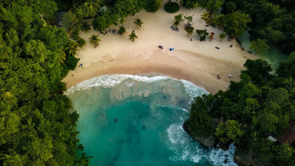 Luchtfoto van een tropisch strand in Jamaica omgeven door groen regenwoud en turquoise zee met golven
