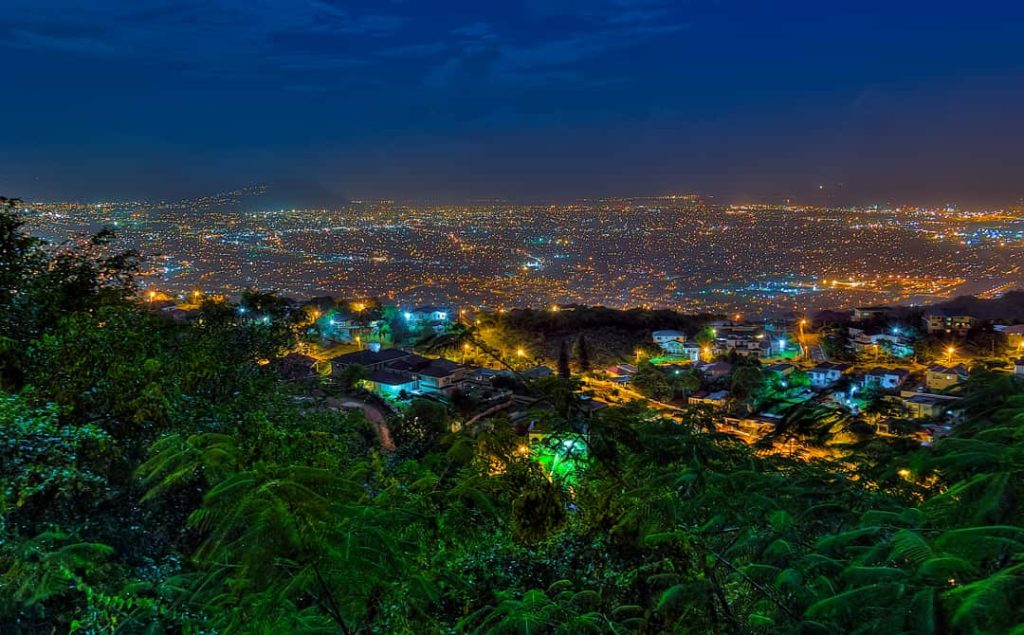 Weids uitzicht bij avond over een verlichte kustplaats in Jamaica, gezien vanaf een beboste heuvel op de voorgrond
