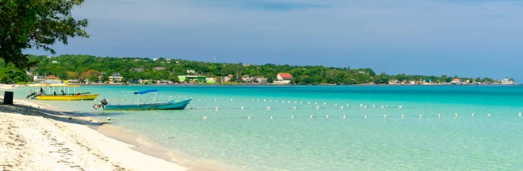 Twee kleine bootjes liggen voor anker op ondiep turquoise water bij een wit zandstrand in Negril