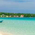 Twee kleine bootjes liggen voor anker op ondiep turquoise water bij een wit zandstrand in Negril