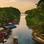Smalle rivier omzoomd door dichte jungle met meerdere kleurrijke houten bootjes aan de oever bij zonsondergang in Jamaica