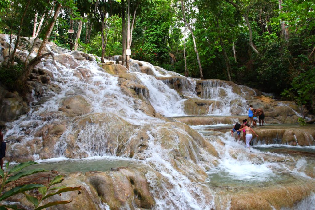 Toeristen klimmen langs de kabbelende watervallen van Dunn's River Falls, omringd door weelderig groen tropisch bos in Jamaica