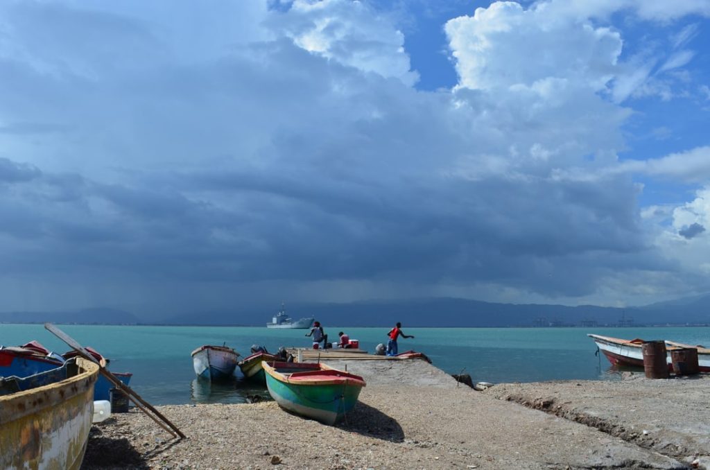 Kleurrijke houten vissersboten liggen op het strand terwijl mensen werken onder een donkere onweerslucht in Jamaica