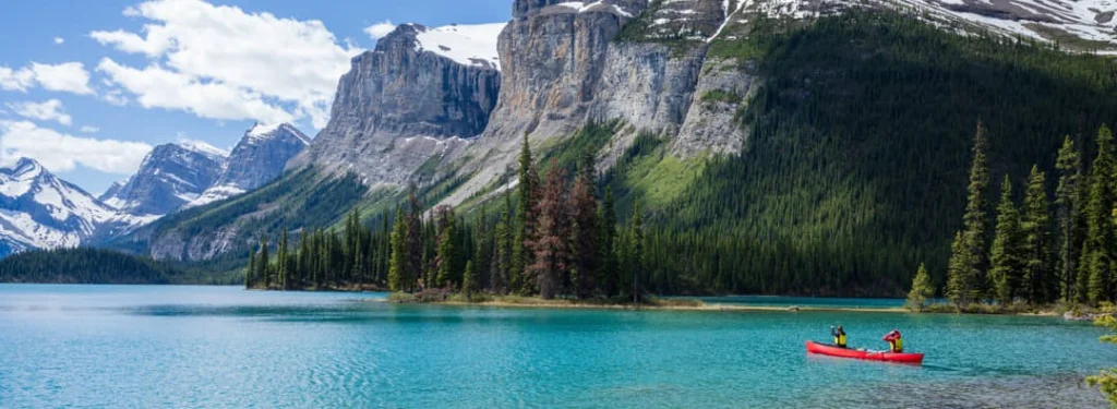 Rode kano met twee mensen op het turquoise water van Maligne Lake, omringd door dennenbossen en steile besneeuwde bergtoppen
