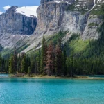 Rode kano met twee mensen op het turquoise water van Maligne Lake, omringd door dennenbossen en steile besneeuwde bergtoppen