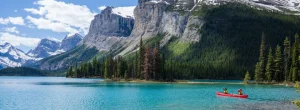 Rode kano met twee mensen op het turquoise water van Maligne Lake, omringd door dennenbossen en steile besneeuwde bergtoppen