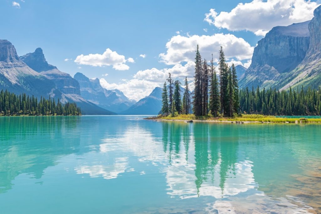 Uitzicht vanaf de oever over het turquoise water van Maligne Lake naar het beboste eilandje Spirit Island met bergtoppen op de achtergrond